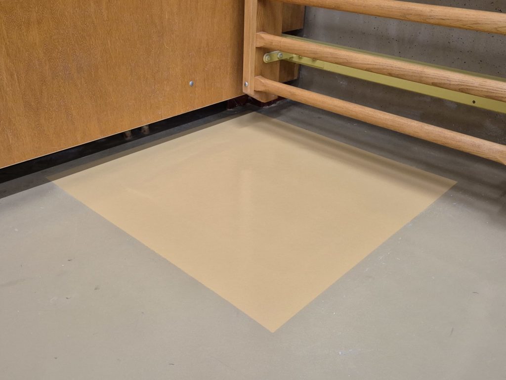 Zone réparée d'un sol de salle de rythmique peinte dans une teinte de base, au pied d'un espalier