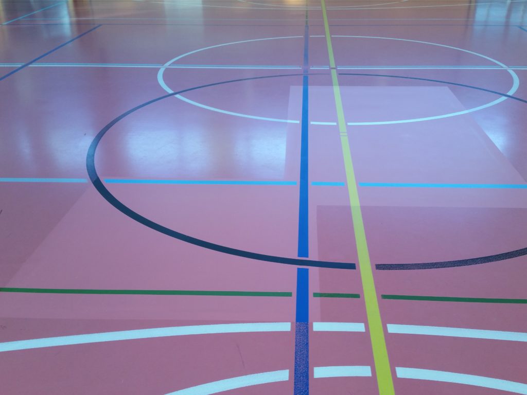 Réparation localisée d'un sol sportif en résine : deux zones découpées et reconstruites, filet de renforcement posé avant la nouvelle résine