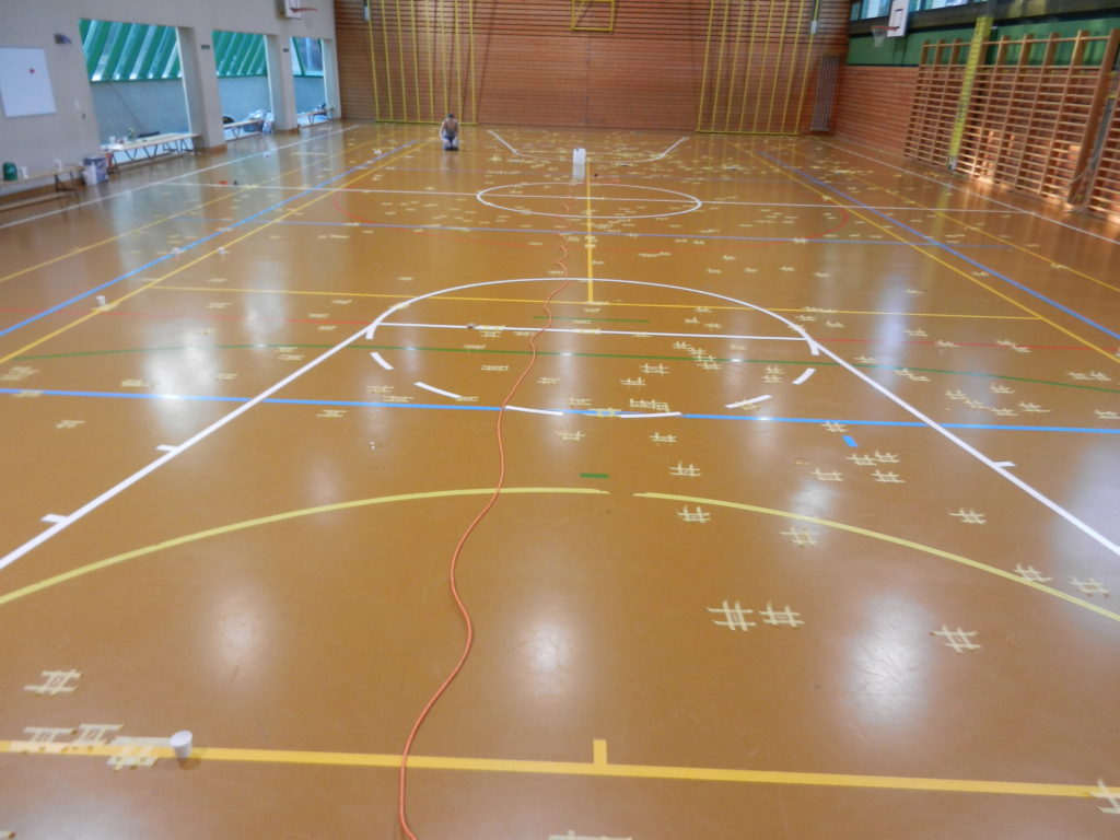 Salle de gymnastique au sol en résine, des centaines de fissures repérées au ruban de masquage sur toute la surface de jeu