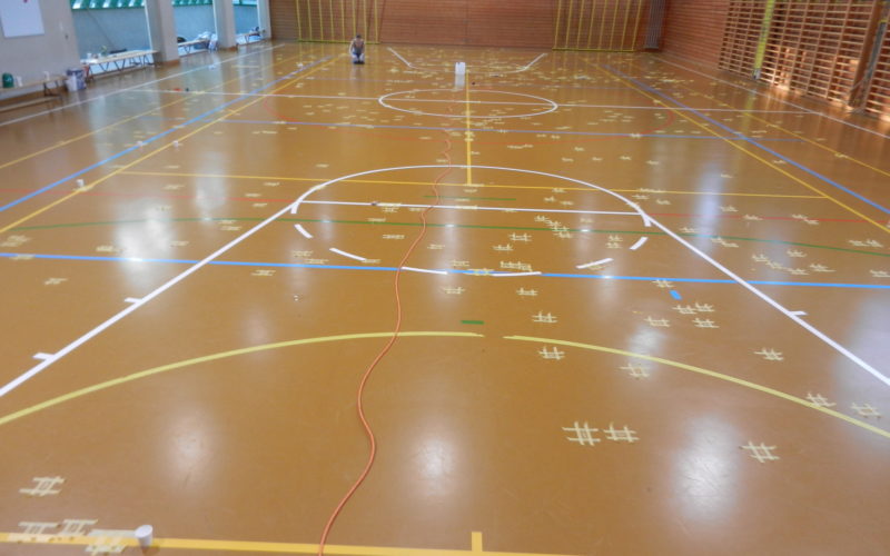 Salle de gymnastique au sol en résine, des centaines de fissures repérées au ruban de masquage sur toute la surface de jeu