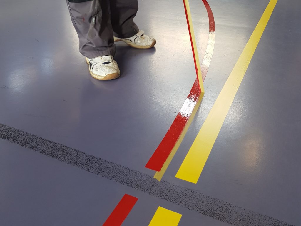 Retrait du ruban le long d'une ligne rouge courbe fraîchement peinte, à côté d'une ligne jaune terminée