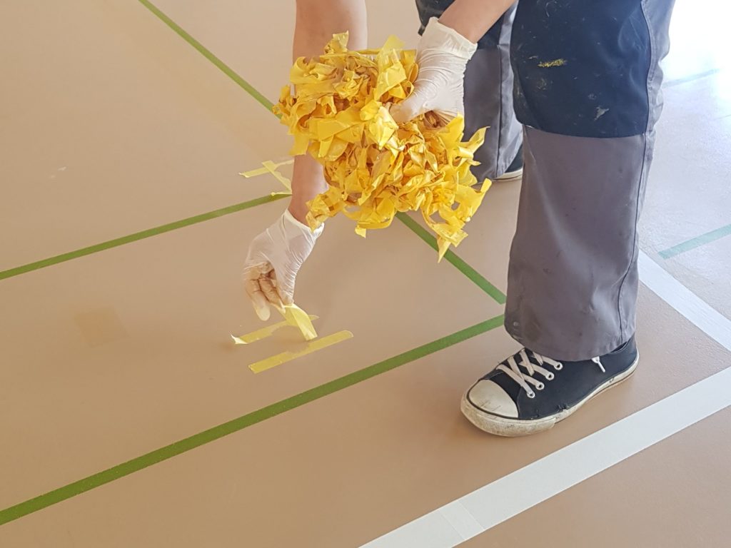 Retrait du ruban de masquage après la reprise en résine des déchirures d'un sol sportif