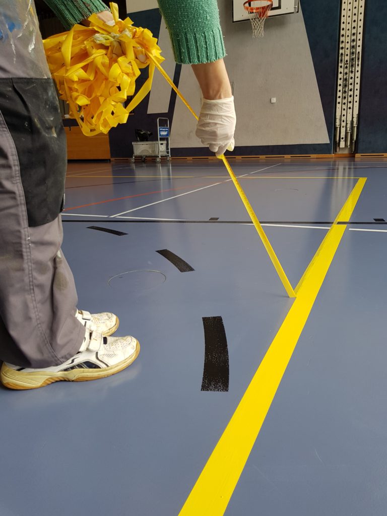 Retrait du ruban de masquage le long d'une ligne jaune fraîchement peinte sur un sol sportif
