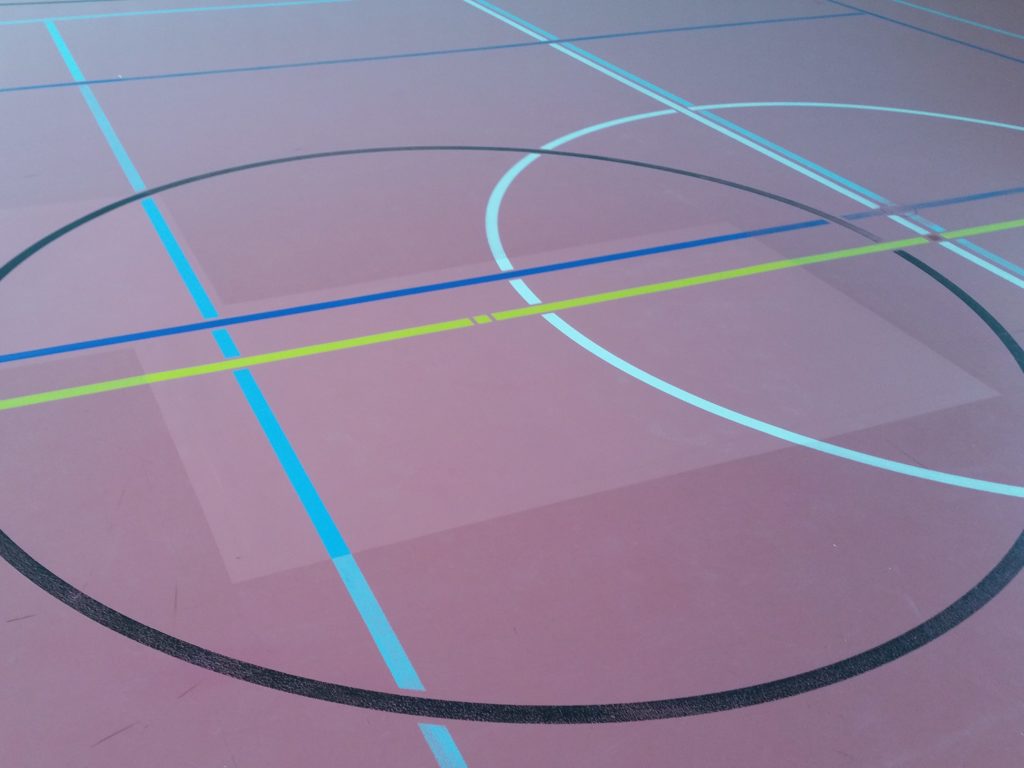 Rond central d'un sol sportif après réfection, revêtement et lignes de jeu repris sur les zones réparées
