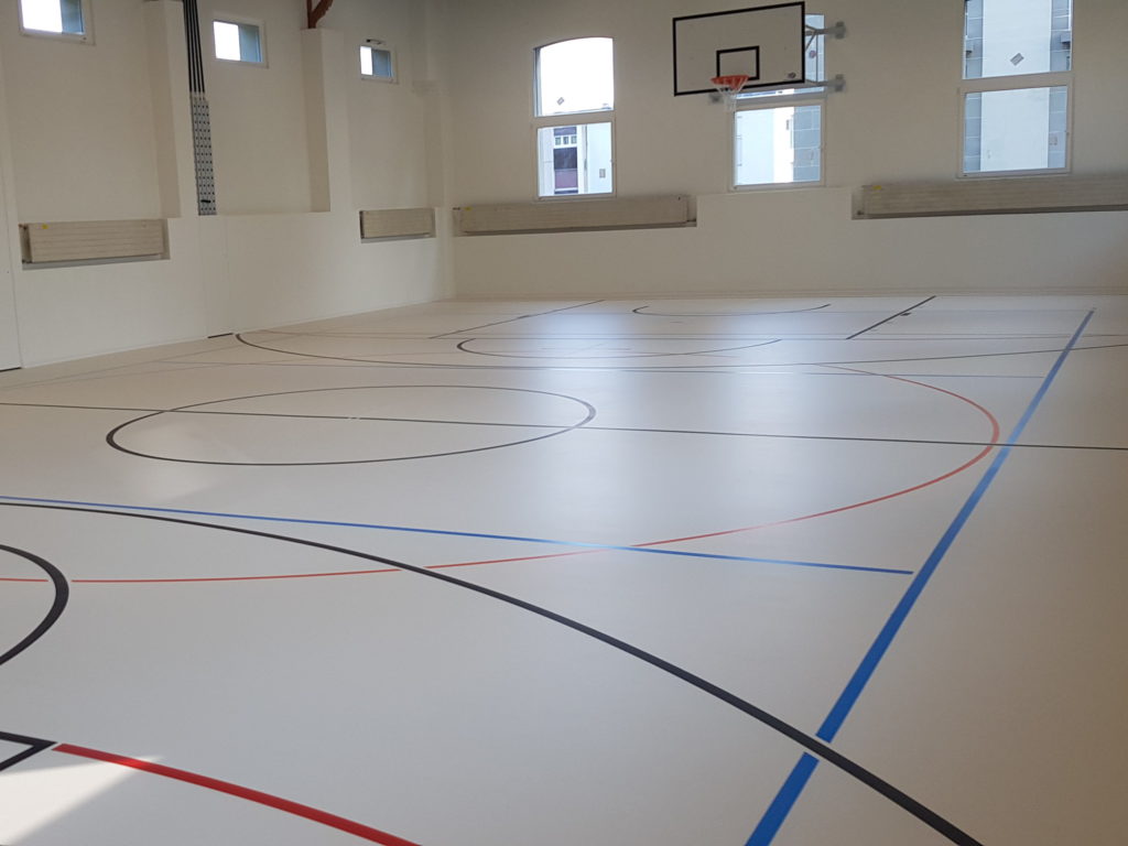 Salle de gymnastique rénovée avec un sol sportif clair et un marquage multisport