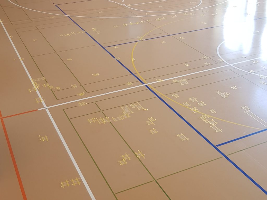 Salle de gymnastique dont les déchirures du sol sont délimitées au ruban de masquage avant leur réparation