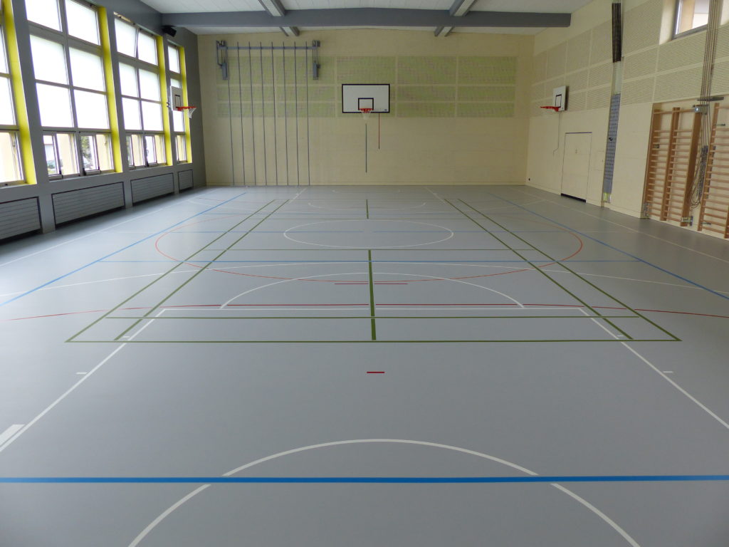 Salle de gymnastique rénovée avec un sol sportif gris clair et un marquage multisport