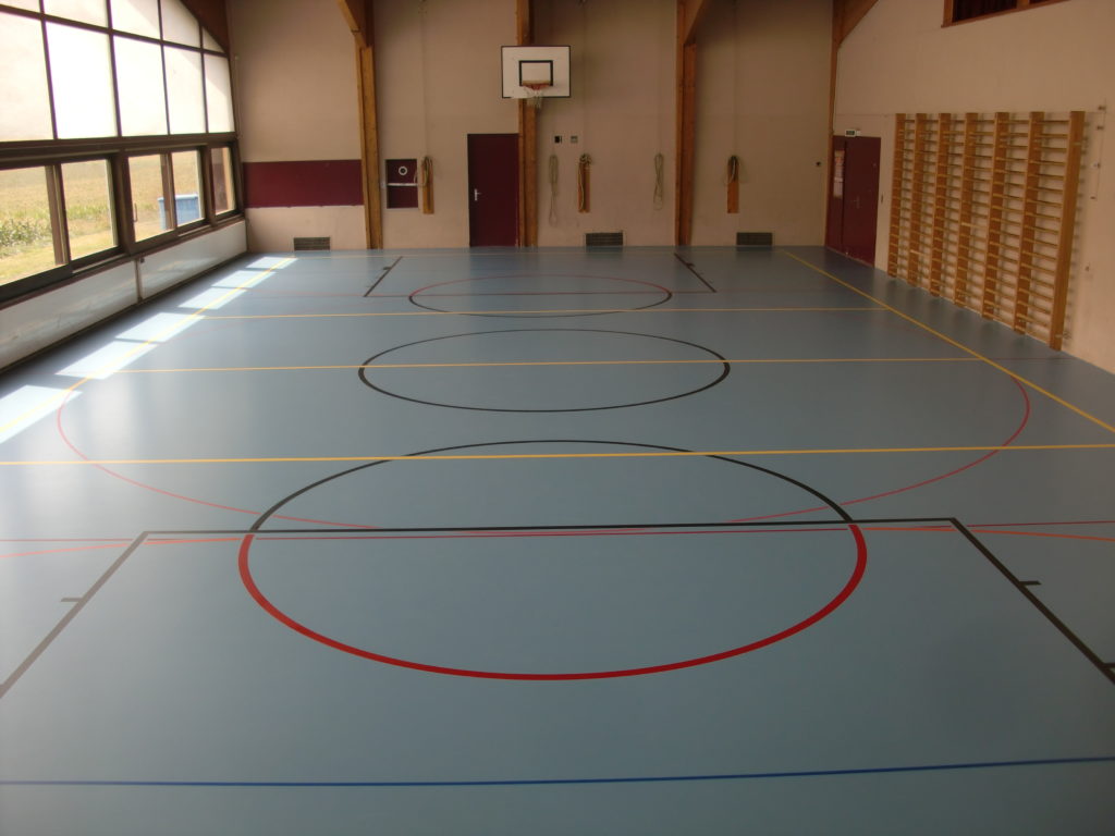 Salle polyvalente rénovée avec un sol sportif bleu et un marquage multisport