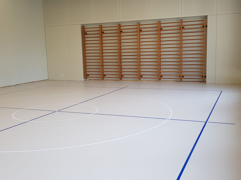 Salle de rythmique rénovée avec un sol sportif en résine clair et des espaliers