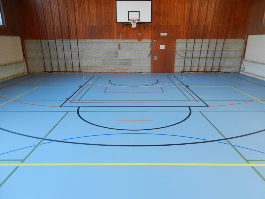 Salle de sport rénovée avec un sol en résine bleu et des lignes de jeu multicolores