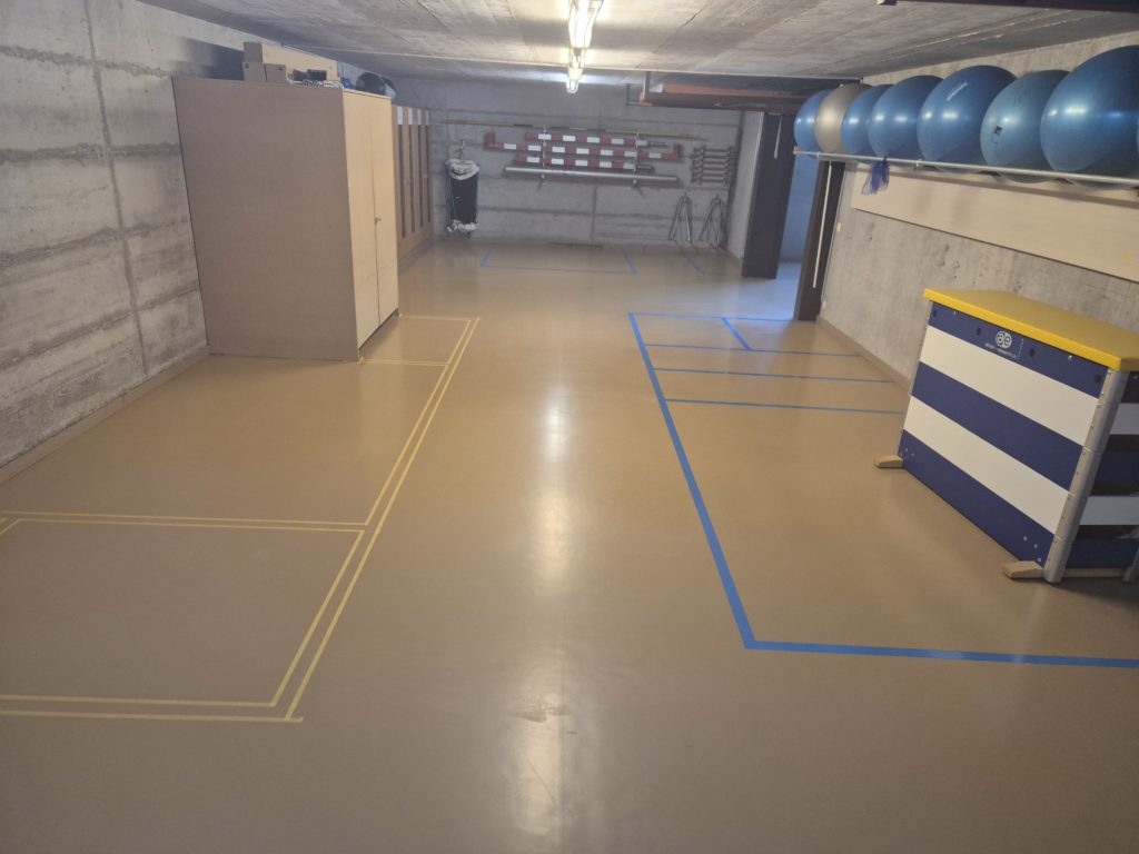 Zone de rangement délimitée au scotch à côté de lignes bleues déjà marquées dans un local à engins