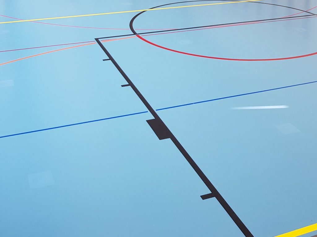 Sol sportif bleu remis en état après assèchement, lignes de jeu intactes et réparations presque invisibles