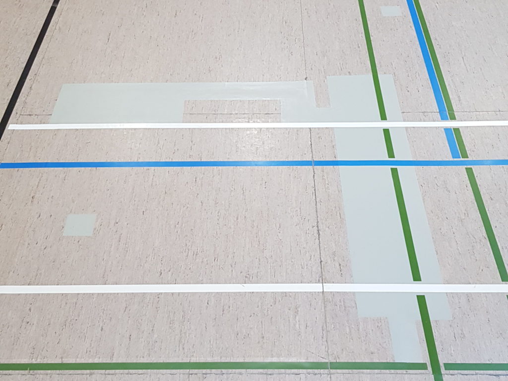 Sol sportif en linoléum après réparation, zones reconstruites refermées et lignes de jeu reprises