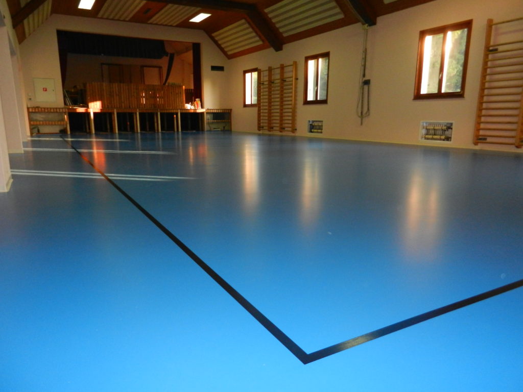Salle polyvalente avec un nouveau sol sportif bleu en résine posé sur une chape chauffante