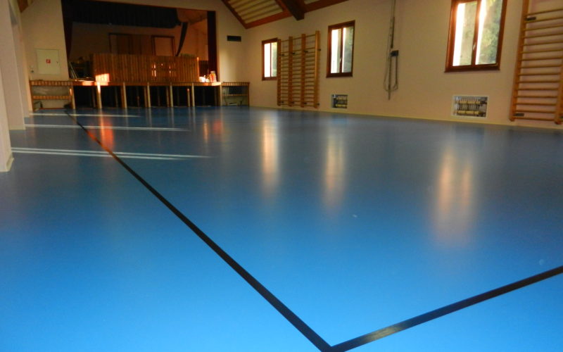 Salle polyvalente avec un nouveau sol sportif bleu en résine posé sur une chape chauffante