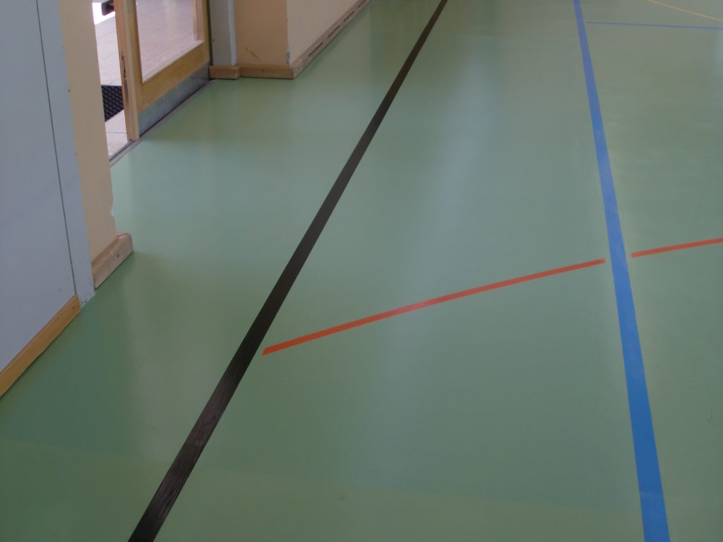 Sol sportif vert après reconstruction d'une zone le long d'une paroi, revêtement et lignes de jeu repris sans raccord visible