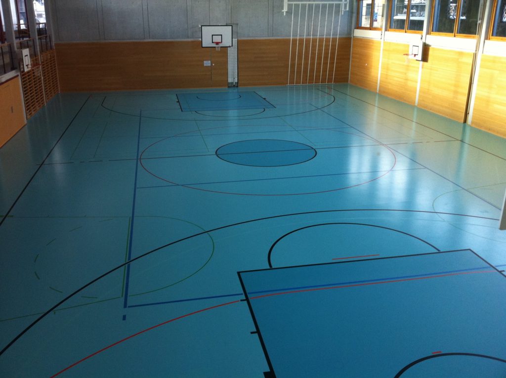 Vue d'ensemble d'une salle de sport avec son terrain de basket bicolore remis aux normes FIBA