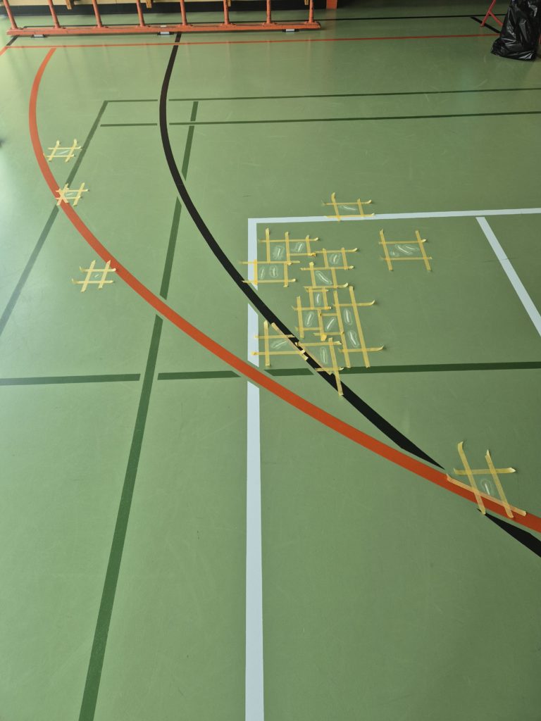 Déchirures d'un sol sportif en résine reprises une à une, chaque zone délimitée par du ruban de masquage