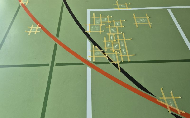 Déchirures d'un sol sportif en résine reprises une à une, chaque zone délimitée par du ruban de masquage
