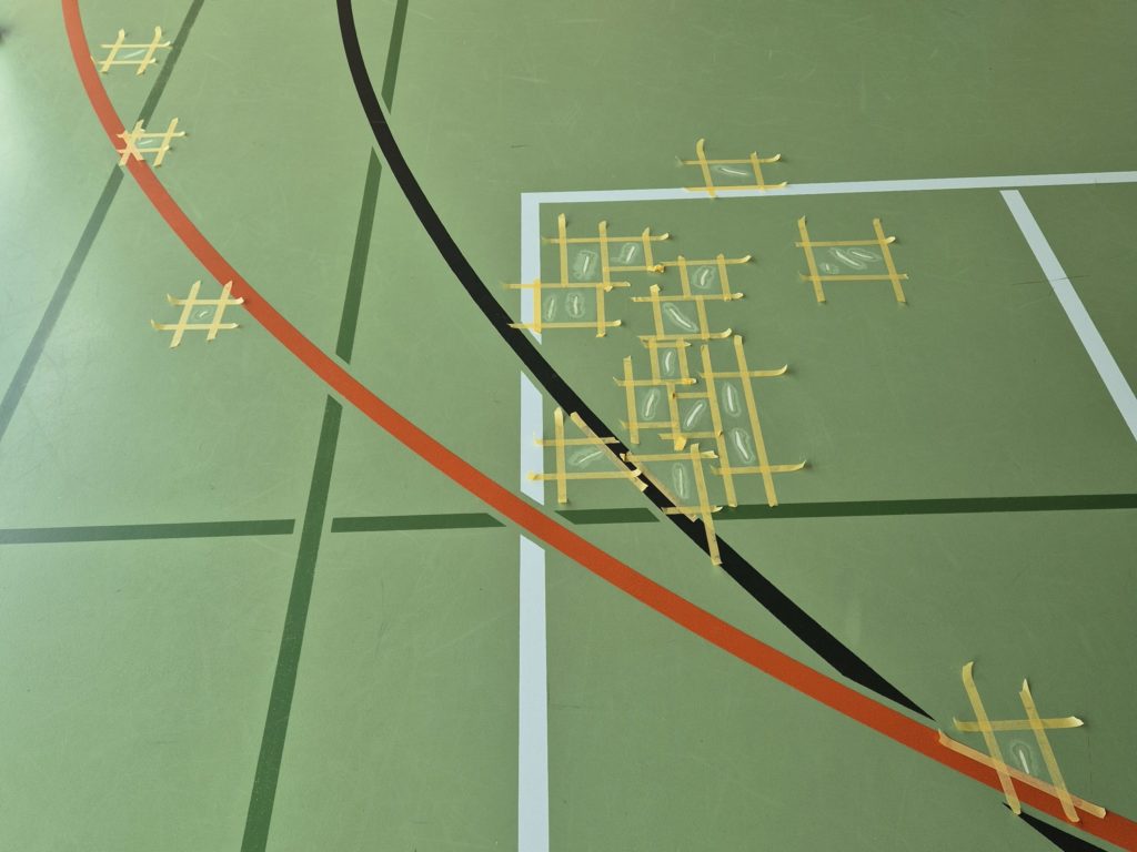 Déchirures d'un sol sportif en résine reprises une à une, chaque zone délimitée par du ruban de masquage