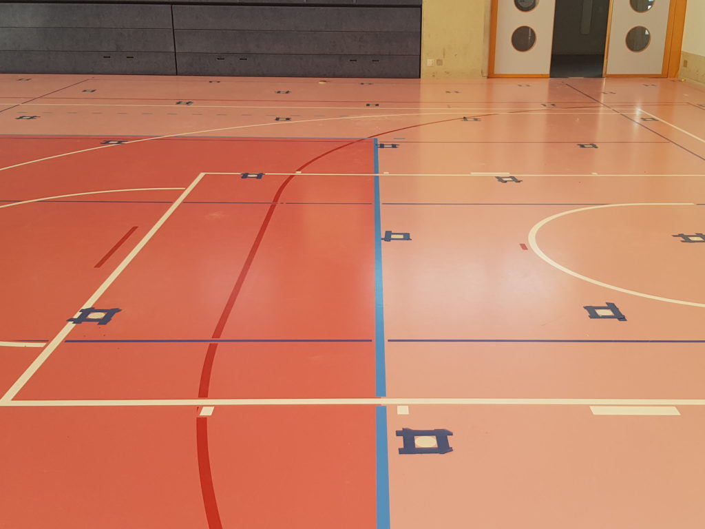 Trous de carottage rebouchés dans toute une salle de sport, chacun cadré au ruban avant la finition