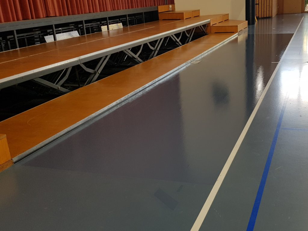 Zone d'un sol sportif dépolie puis repeinte en polyuréthane devant la scène d'une salle polyvalente
