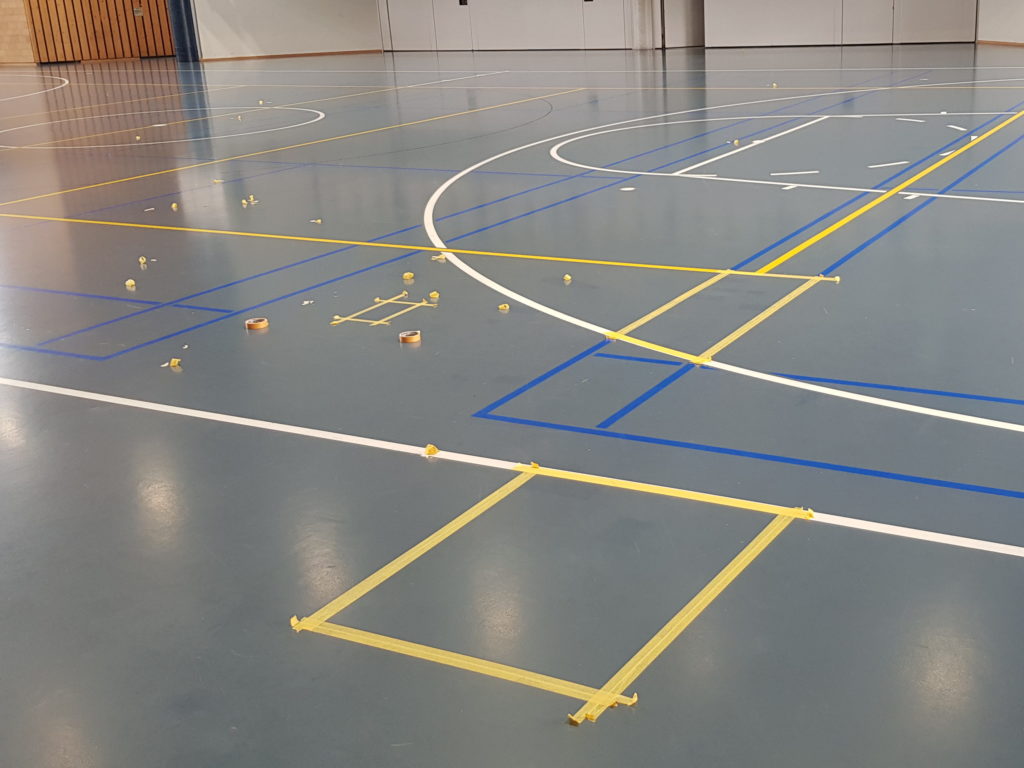 Zones d'un sol sportif délimitées au ruban de masquage avant leur traitement, dans une salle polyvalente