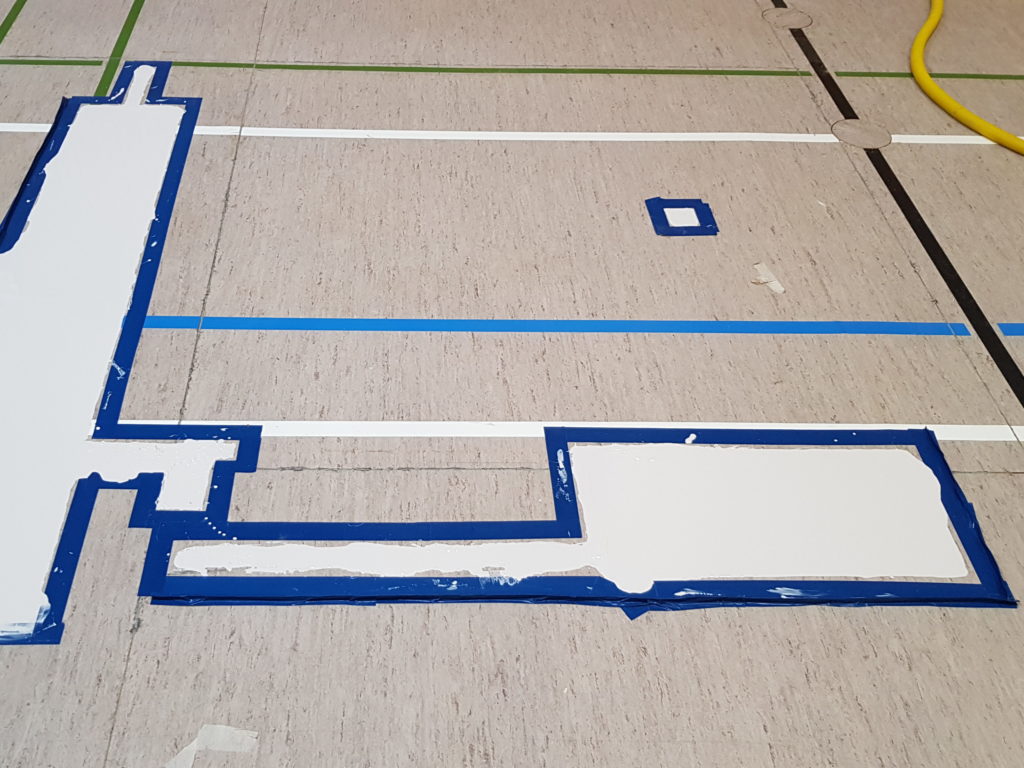 Zones de sol sportif refermées et enduites dans leur découpe, cadrées au ruban avant la finition
