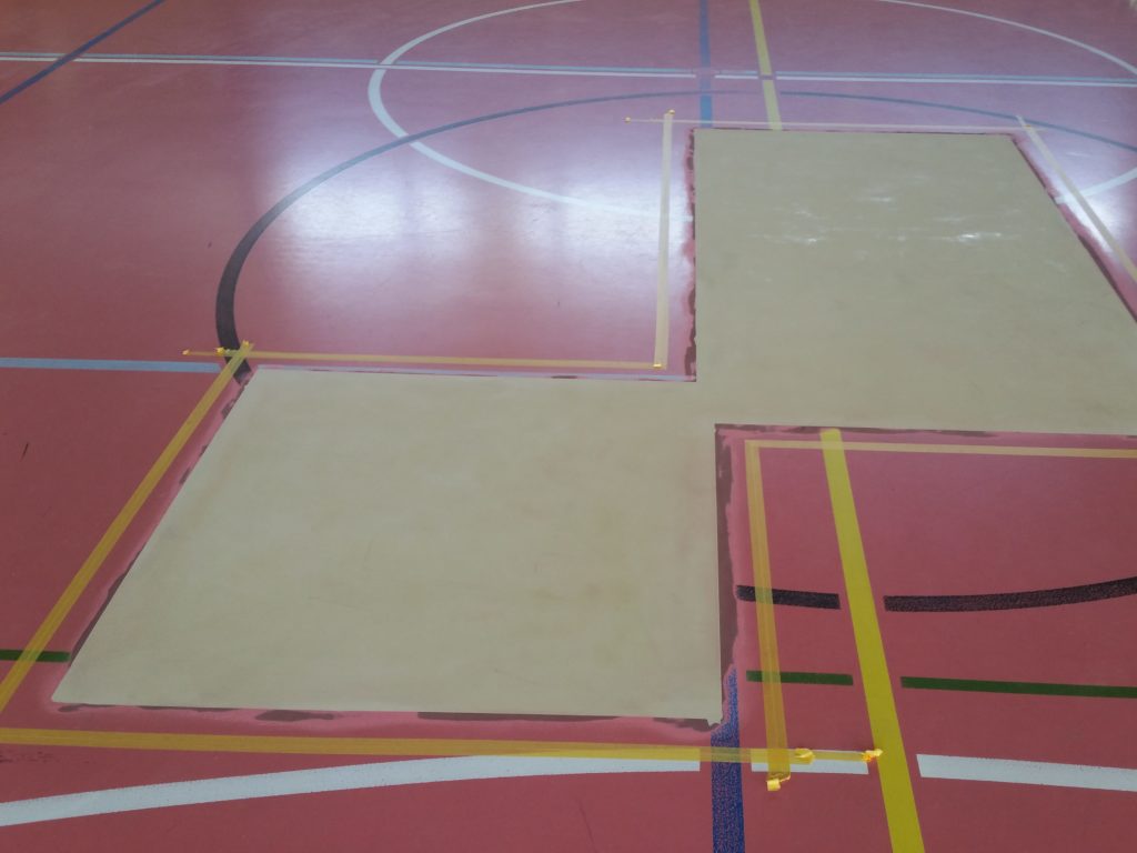 Zones réparées d'un sol sportif mises à niveau et cadrées au ruban, prêtes pour la peinture de sol