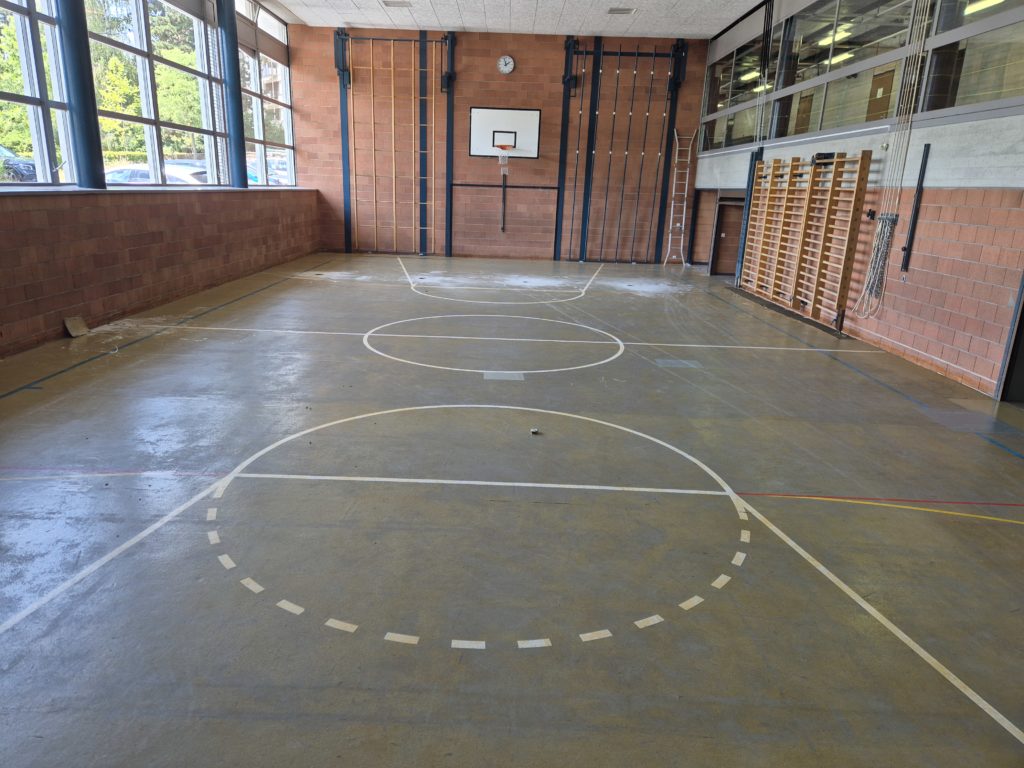 Ancien revêtement en lino-liège usé et taché dans une salle de gymnastique, avant son remplacement par un sol sportif
