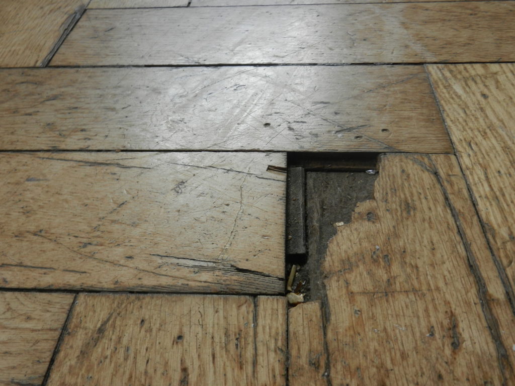 Lame de parquet cassée, avec un morceau manquant qui laisse voir le support en dessous.