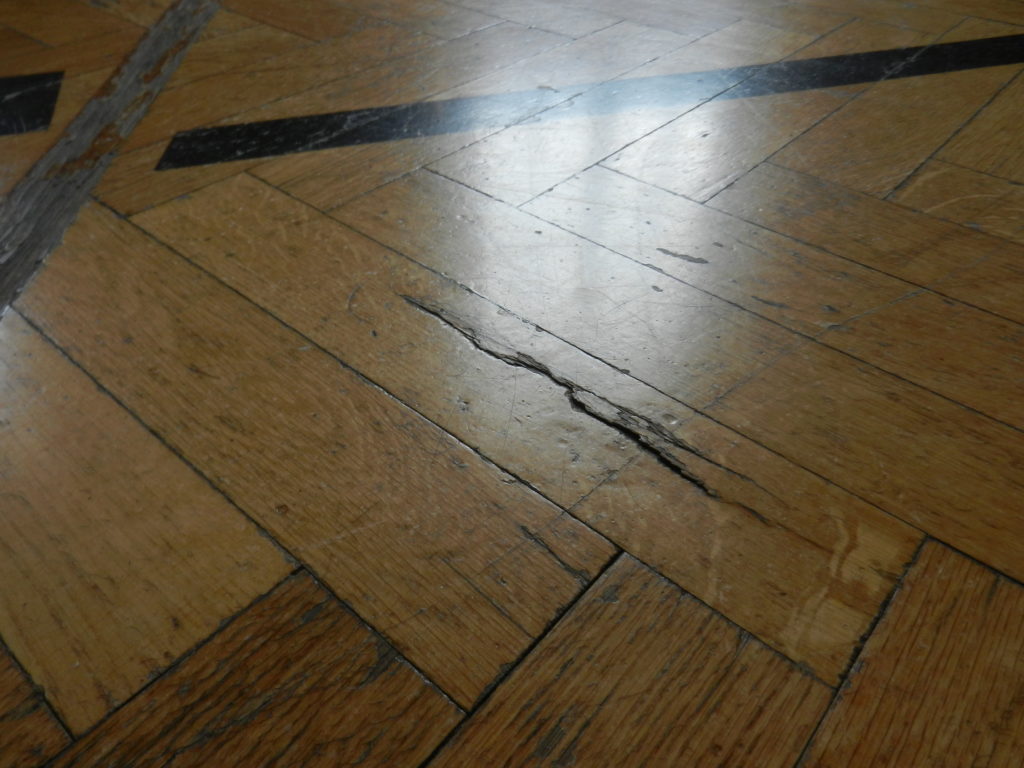 Lame de parquet en chêne fendue et éclatée dans la longueur, près d'une ligne de jeu noire.