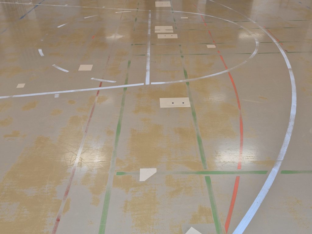 Constat d'usure sur un sol sportif en résine PU : peinture partie par plaques et lignes effacées.