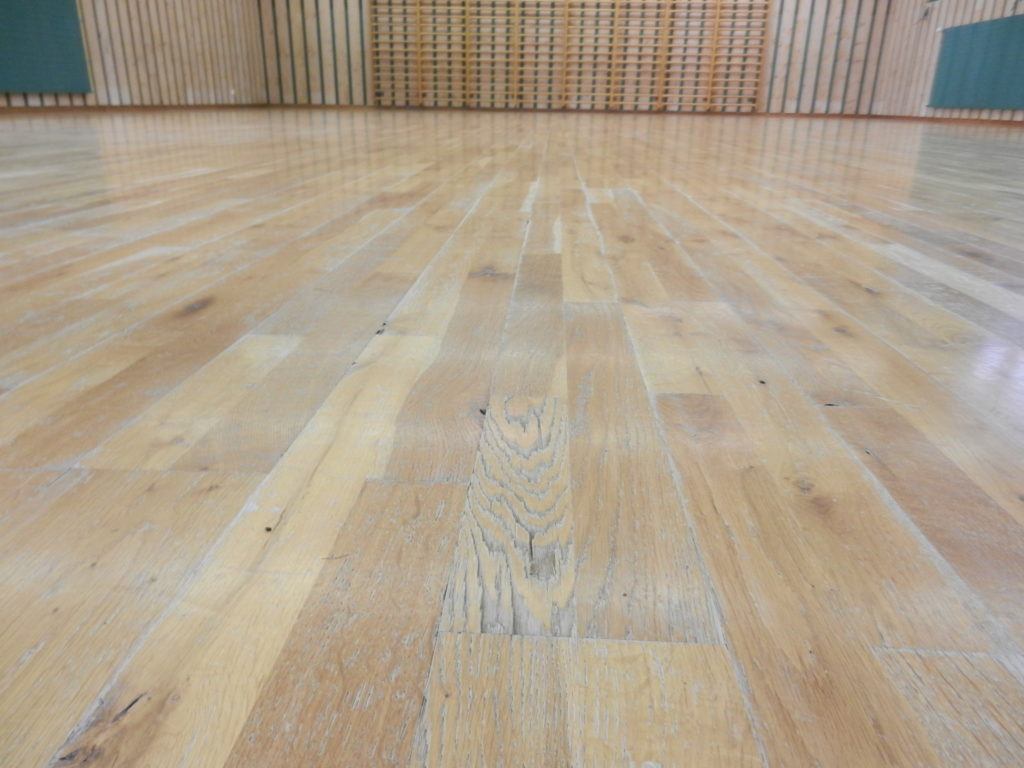 Gros plan d'une vitrification cassante sur parquet en chêne : film éclaté et blanchi le long du fil du bois.