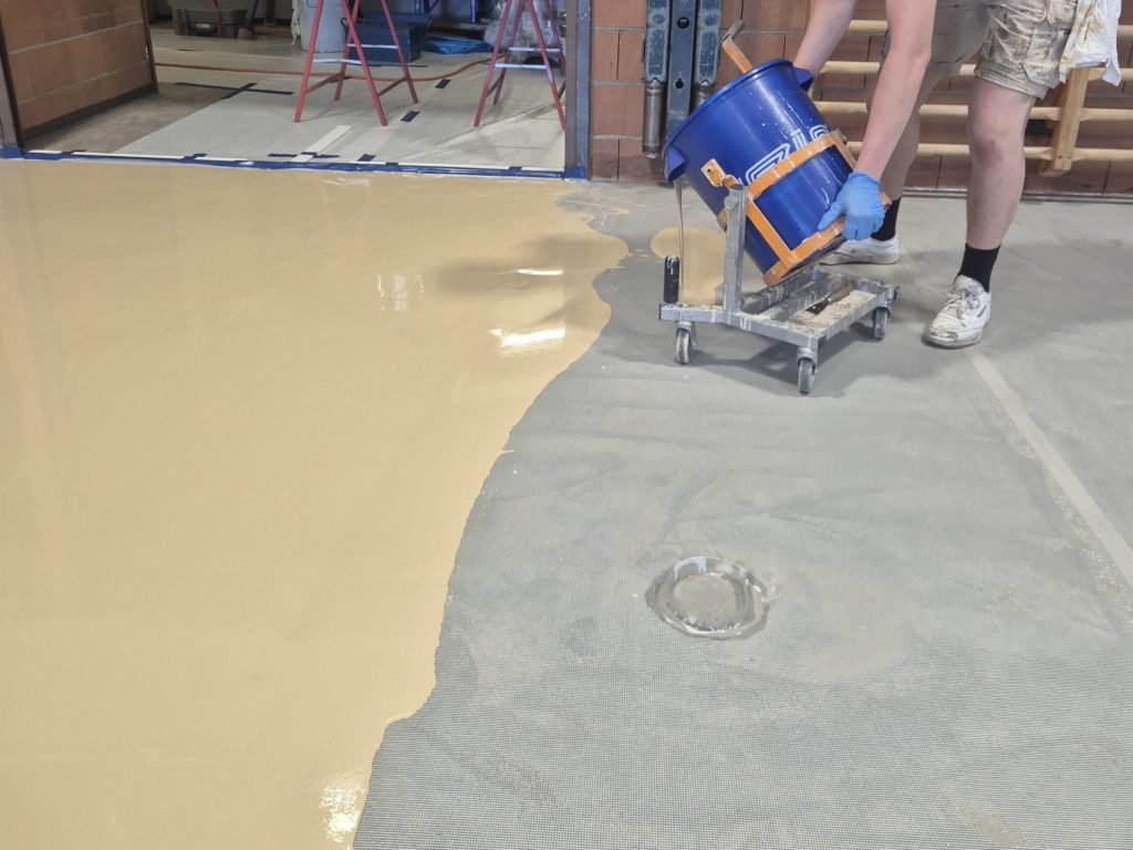 Coulage de la résine polyuréthane beige du sol sportif ProtecSport SP 40 sur le filet de renforcement spatulé