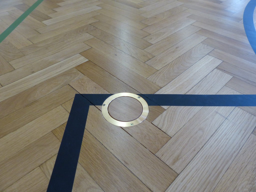 Douille de sol en laiton et angle de ligne de jeu noire sur le parquet vitrifié.