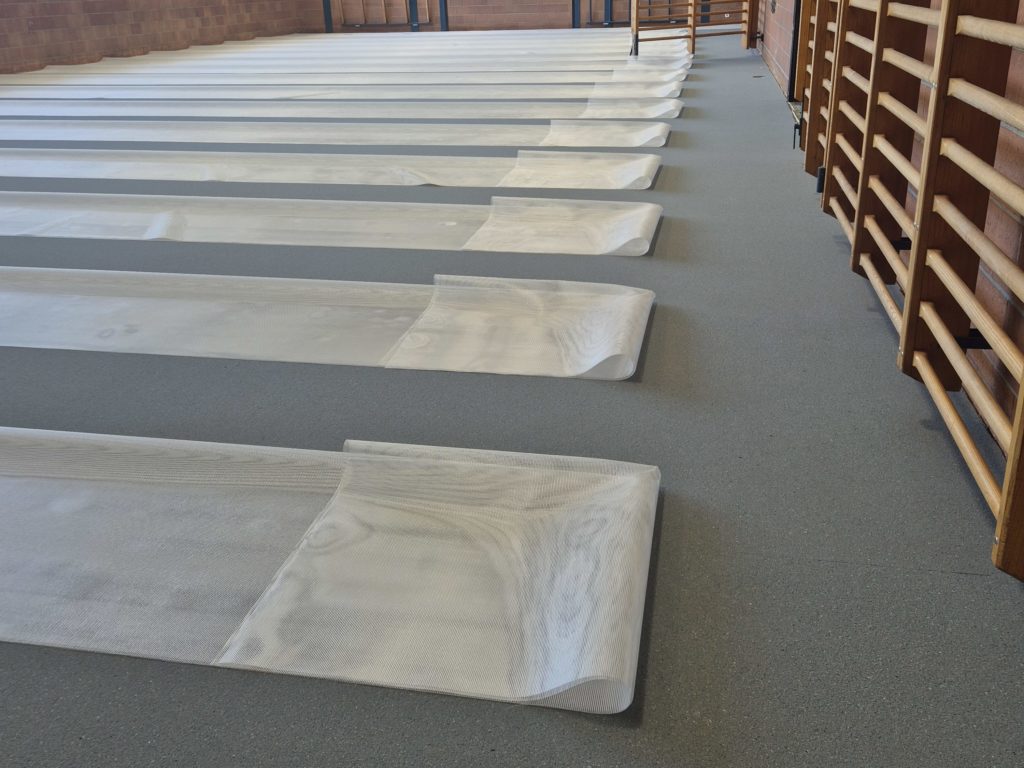 Sous-couche grise posée dans une salle de gymnastique, lés de filet de renforcement déroulés avant le spatulage
