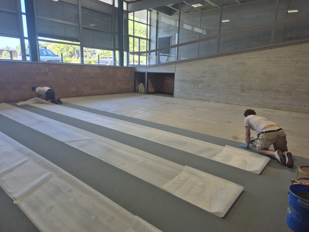 Pose du filet de renforcement sur la sous-couche d'un sol sportif dans une salle de rythmique, noyé par spatulage