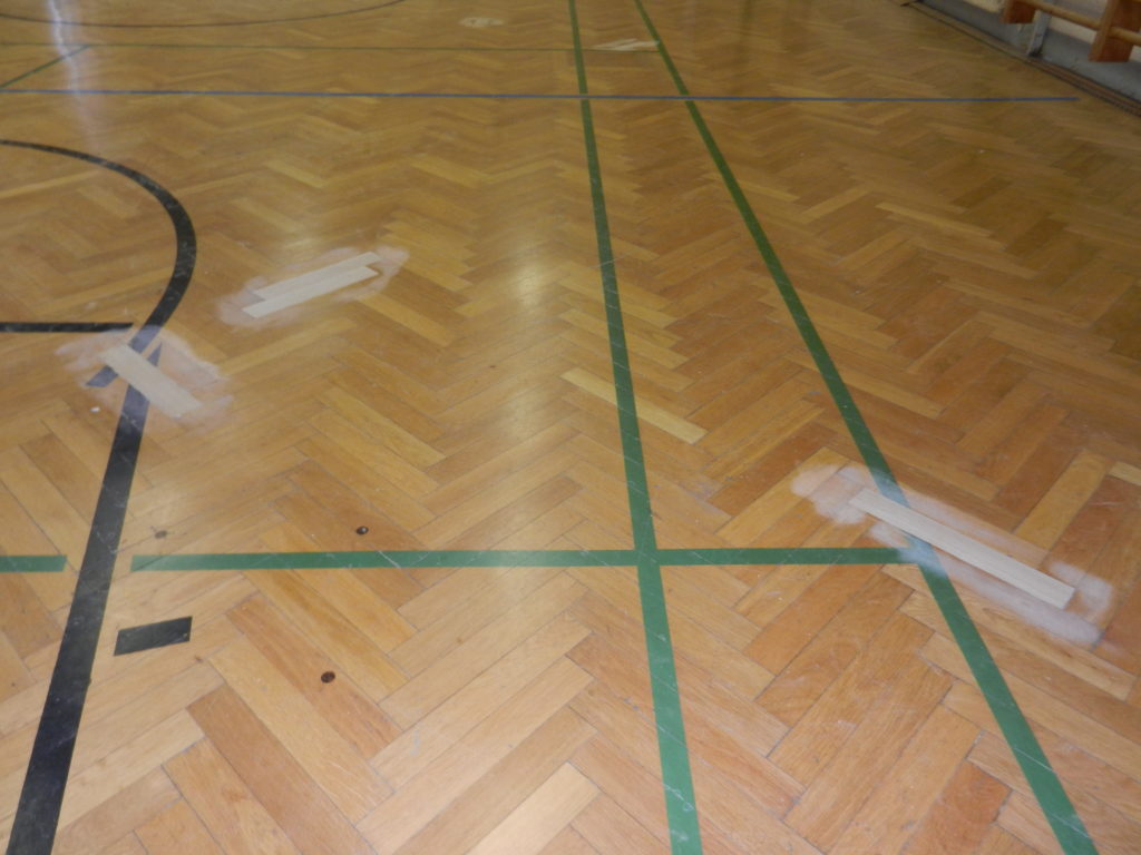 Lames neuves, plus claires, posées à la place des lames abîmées dans le parquet en bâtons rompus.