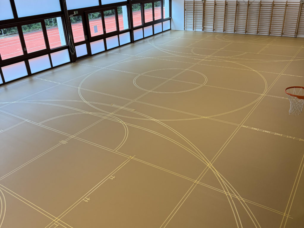 Marquage d'un sol sportif : toutes les lignes de jeu implantées au scotch avant la peinture, vue d'ensemble de la salle