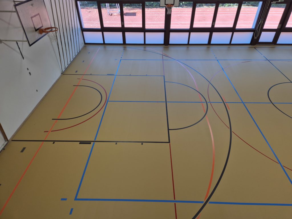 Lignes de jeu terminées près du panier de basket, vue plongeante sur le sol sportif rénové.