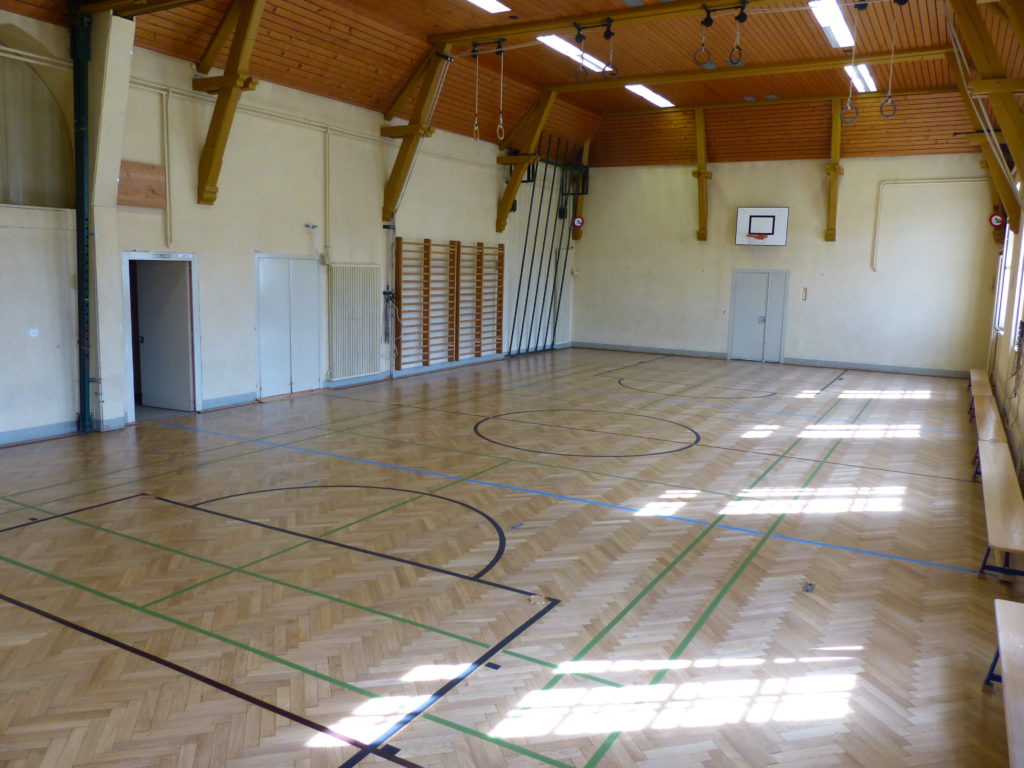 Salle de gymnastique au parquet en chêne en bâtons rompus rénové, avec un marquage pour plusieurs sports.