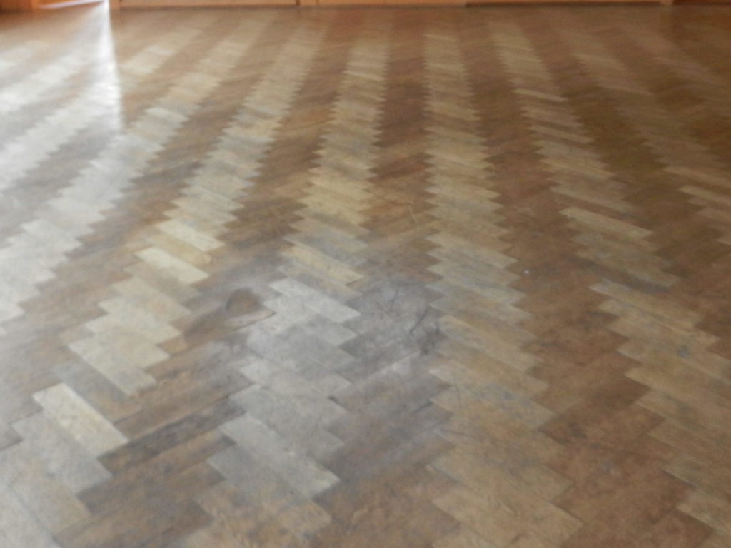 Ancien parquet en chêne posé en bâtons rompus avant rénovation, bois foncé, usé et taché.