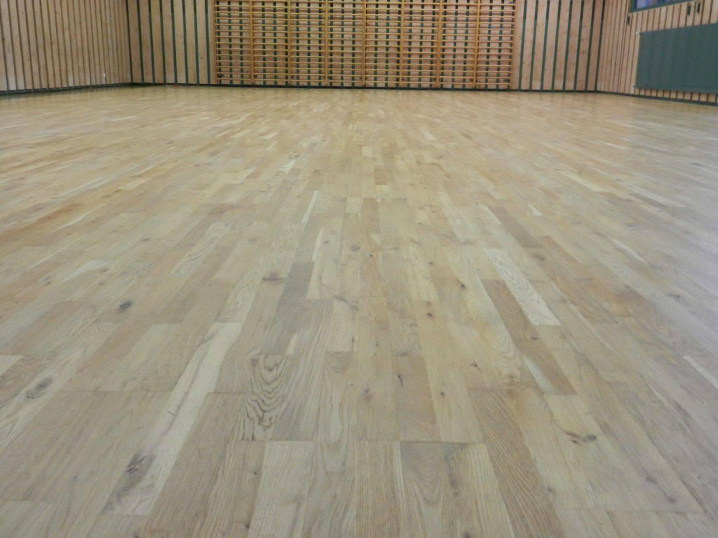 Parquet sportif en chêne après ponçage et vitrification, vue rasante sur la salle.