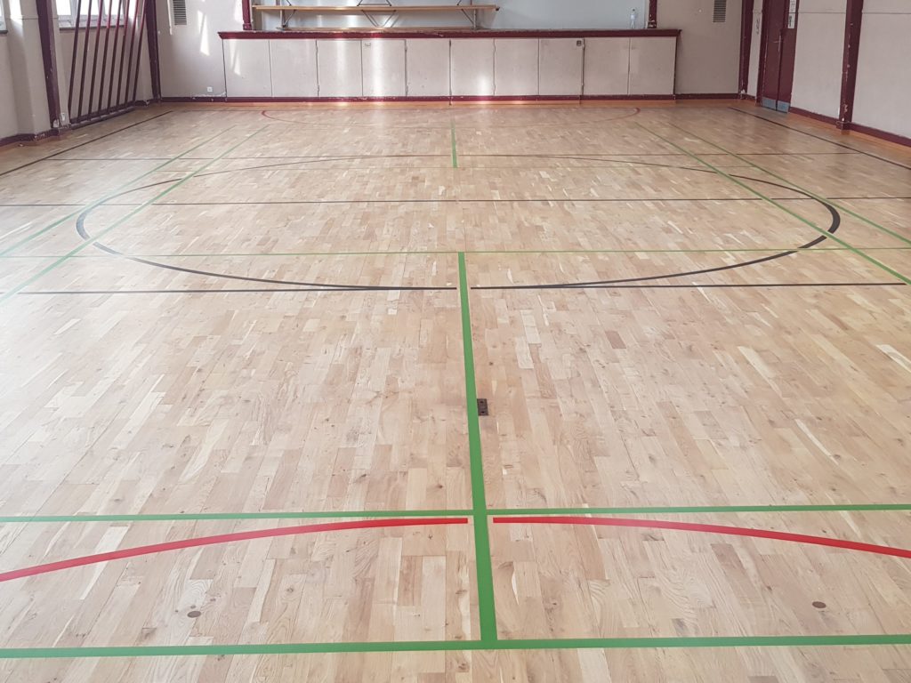 Parquet sportif en chêne poncé et vitrifié, avec un nouveau marquage vert, noir et rouge.