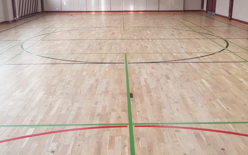 Parquet sportif en chêne poncé et vitrifié, avec un nouveau marquage vert, noir et rouge.
