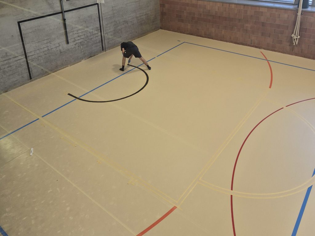 Peinture du marquage d'un sol sportif ProtecSport SP 40 : arc noir peint entre deux bandes de scotch dans une salle de gymnastique