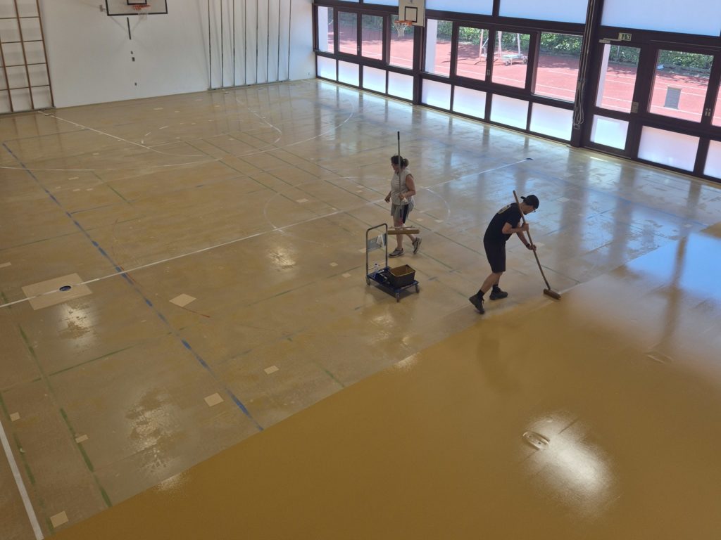 Deux techniciens appliquent la peinture de sol à la raclette sur le sol sportif dépoli.
