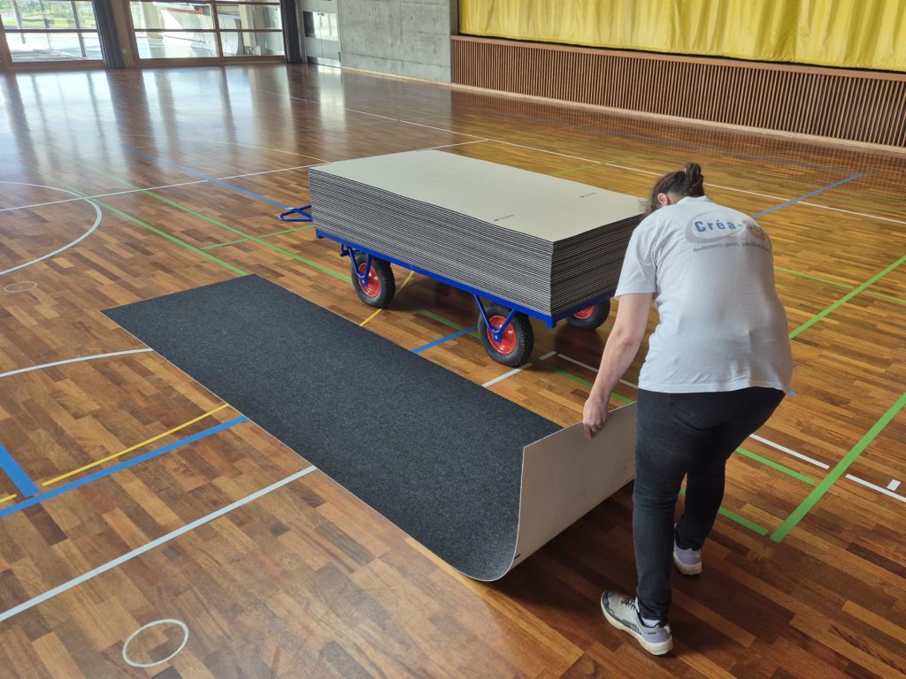 Pose de la protection d'un sol sportif : dalles déroulées sur le parquet depuis un chariot de transport