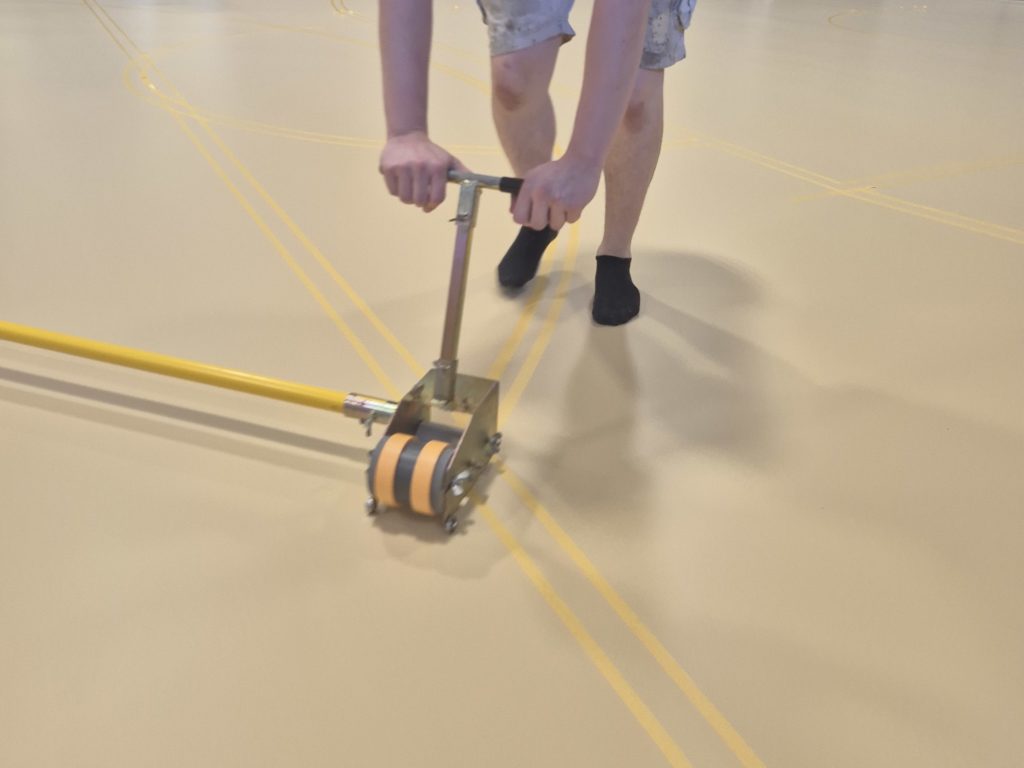 Pose du scotch de marquage à l'applicateur sur un sol sportif en résine, avant la peinture des lignes